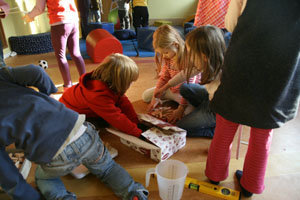 zwei auf dem Boden sitzende Kinder holen Lamello Dübel aus einer Pappschachtel
